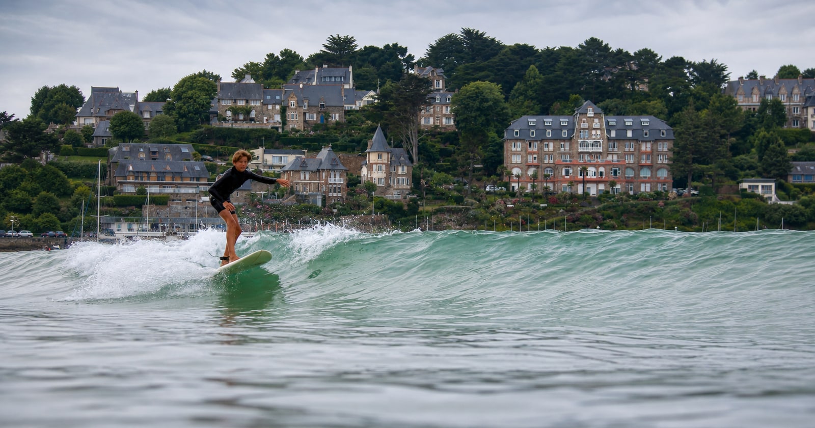 A surfer riding a small summer wave at Trestraou, with the Perros-Guirec seafront in the background